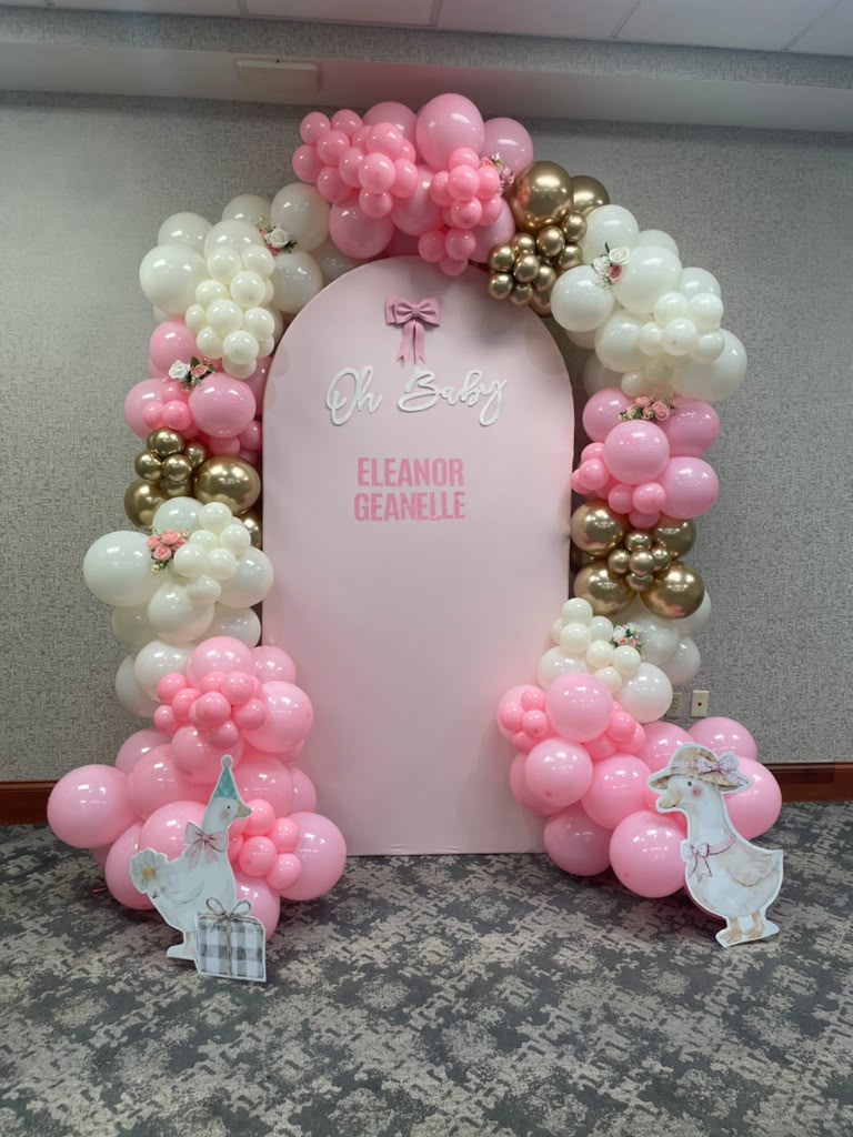 Pink, ivory and gold balloon arch surrounding a personalized baby shower backdrop